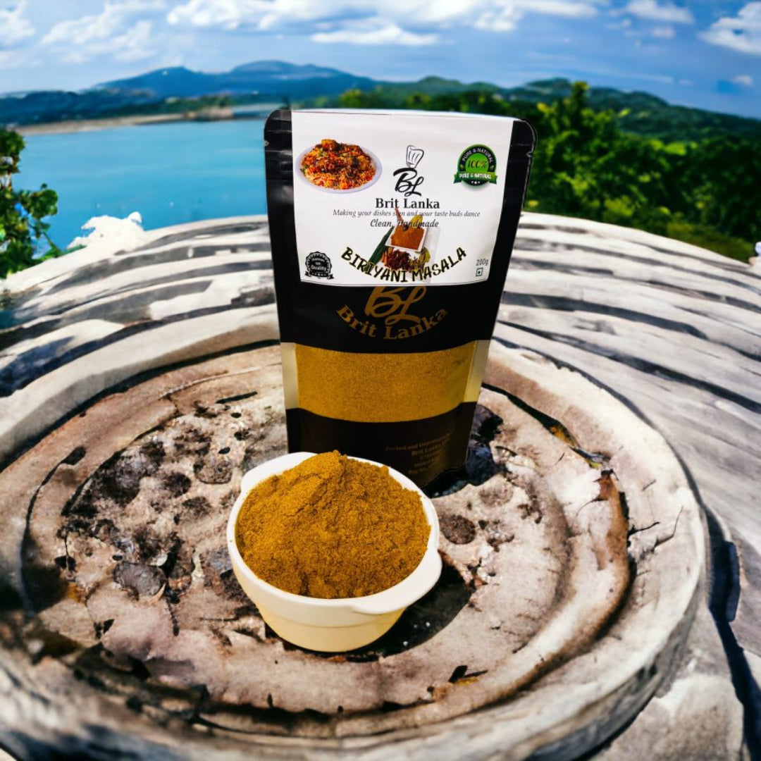 Packaging of BritLanka Homemade Biryani Masala Spice Blend with a small bowl of the spice mix in front, placed on a stone surface with a scenic view in the background.