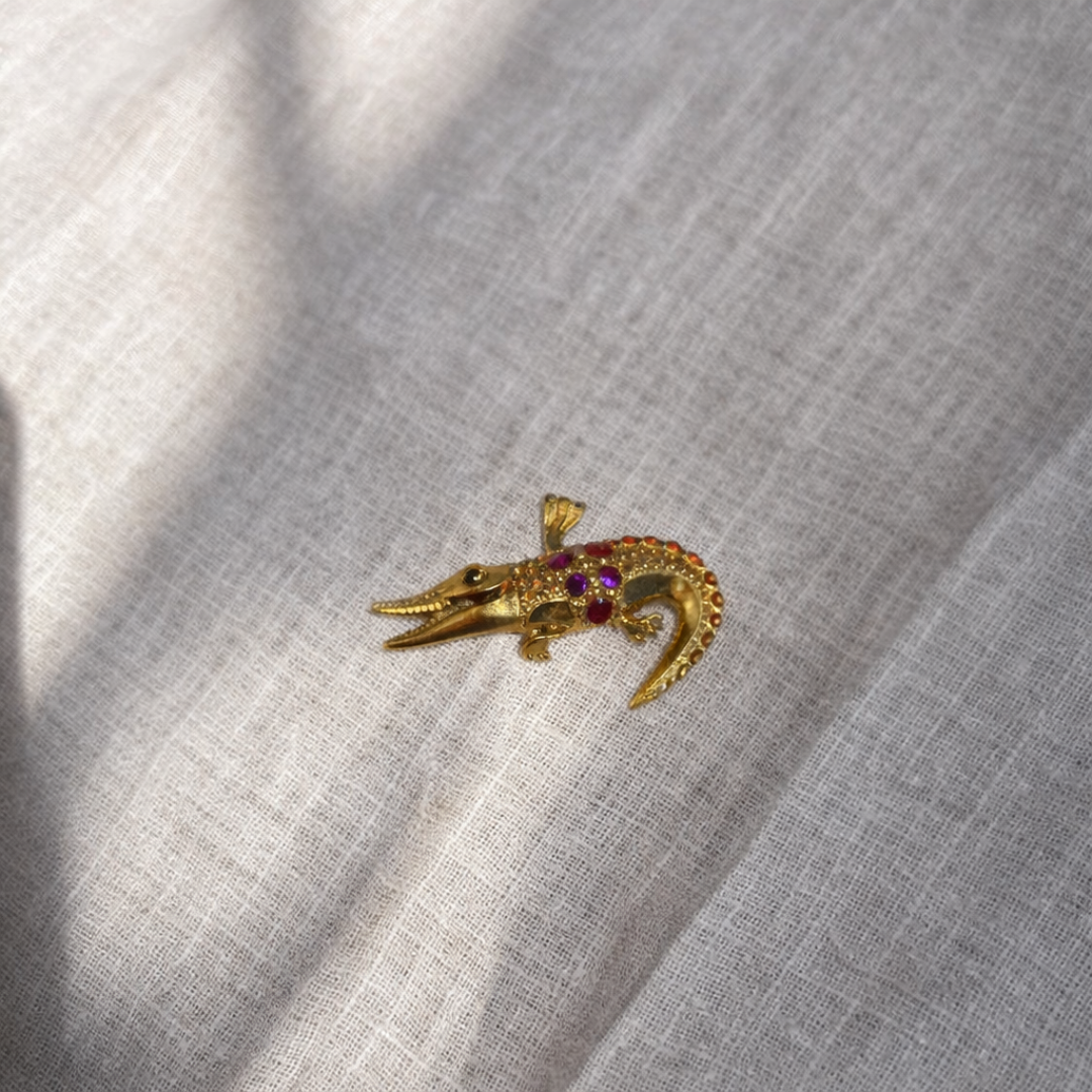 Gold alligator-shaped brooch with red gemstones on a light gray fabric background