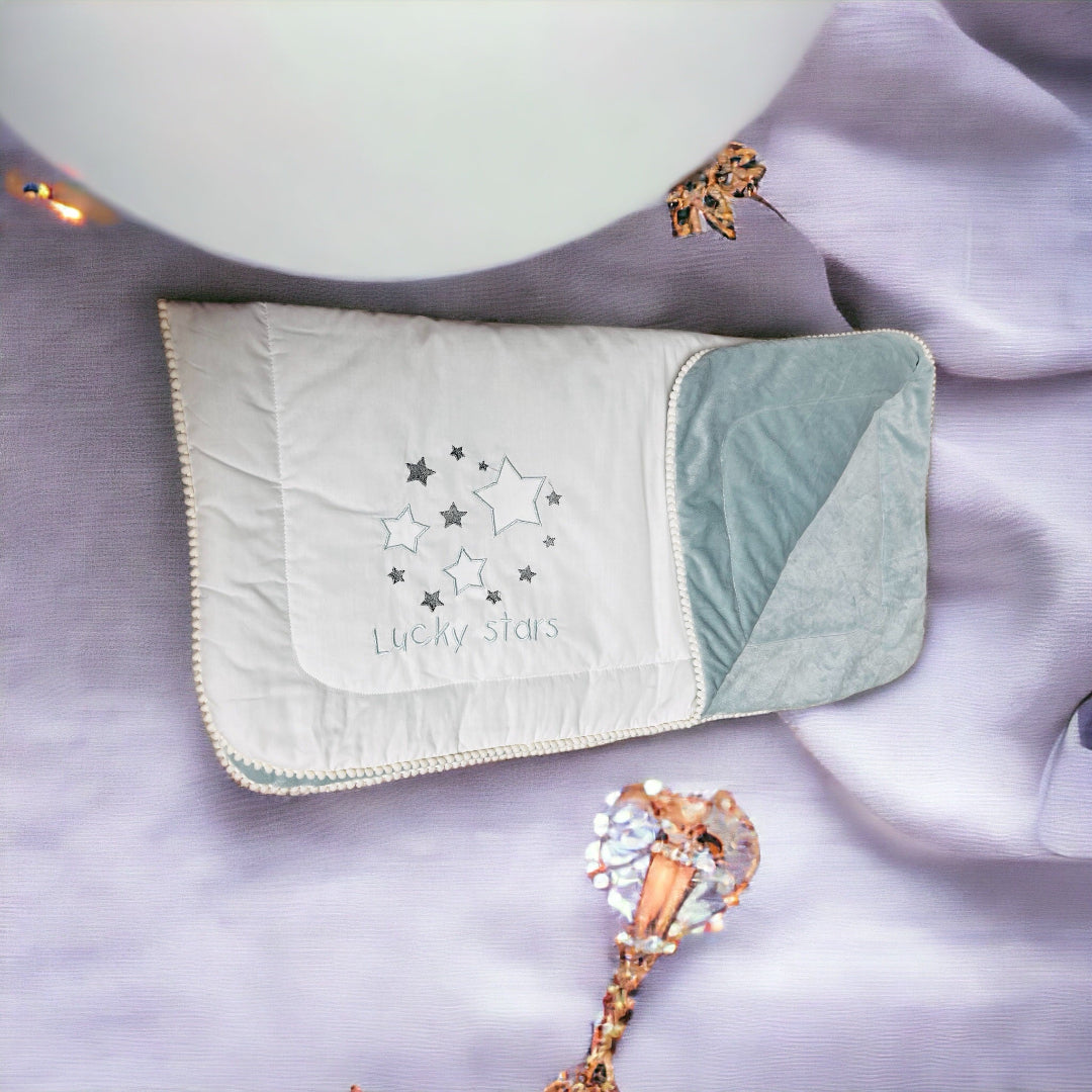 A folded white baby blanket with blue trim and a star pattern, displayed on a purple surface alongside a decorative balloon and a toy.