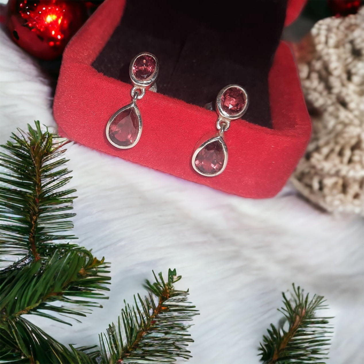 A pair of silver 925 earrings with spessartite stones displayed in a red box with decorative foliage around.